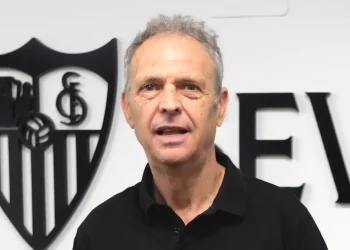 Joaquín Caparrós con el escudo del Sevilla detrás de él. | Imagen: Página web Sevilla FC.