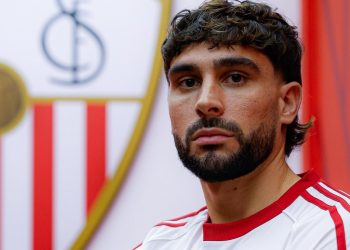 Neal Maupay posando con la camiseta del Sevilla y el escudo al fondo. | Imagen: perfil de X @SevillaFC.