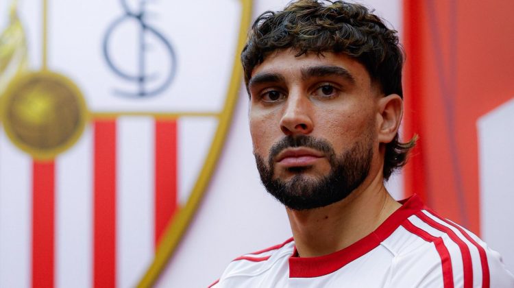 Neal Maupay posando con la camiseta del Sevilla y el escudo al fondo. | Imagen: perfil de X @SevillaFC.