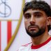 Neal Maupay posando con la camiseta del Sevilla y el escudo al fondo. | Imagen: perfil de X @SevillaFC.